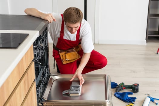 Concept maintenance service of home appliances. Worker cleans filter in the dishwasher. Male repairman checking food residue filters.