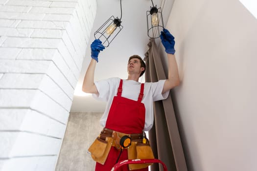 Electrician in uniform installing ceiling lamp indoors. Space for text.