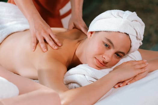 Beautiful young woman received a back massage on a spa bed from professional masseuse. Attractive female relaxes deeply by skilled hands of the massage therapist. Surrounded with nature. Tranquility.