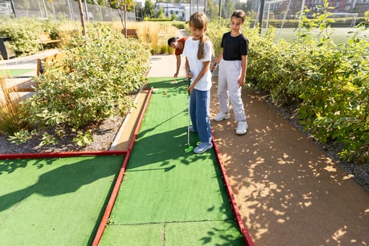 Cute school girl playing mini golf with family. Happy toddler child having fun with outdoor activity. Summer sport for children and adults, outdoors. Family vacations or resort. High quality photo