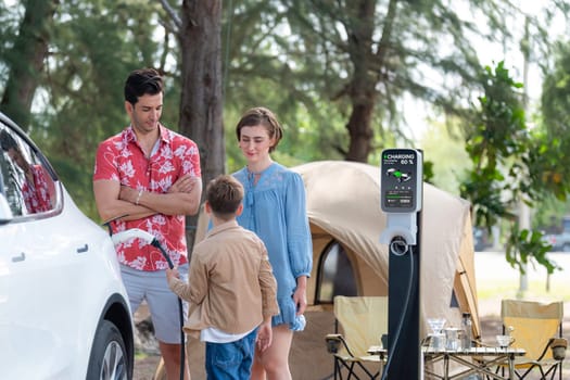 Outdoor adventure and family vacation camping in nature travel by eco friendly car for sustainable future. Lovely family recharge EV car with EV charging station in campsite. Perpetual