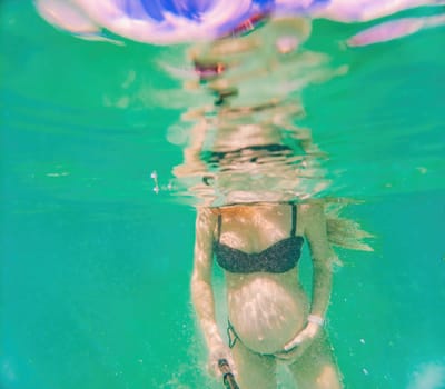 In an ethereal underwater scene, a pregnant woman gracefully floats, embodying the beauty of maternity beneath the tranquil surface of the sea.