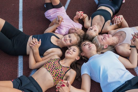 Group of tired and happy fit young girls resting on floor at stadium