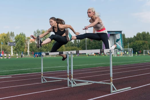 Two athlete woman runnner running hurdles at the stadium outdoors