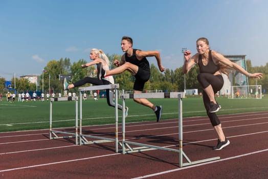 Two athlete woman and man runnner running hurdles at the stadium outdoors