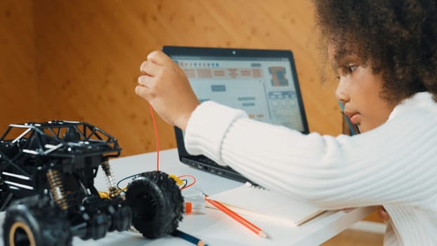 Smart african girl build robotic car while using wires while using laptop setting or writing prompt code. Skilled female student working on computer in STEM technology online classroom. Erudition.