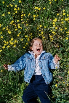 Little laughing girl lies on a green meadow with yellow dandelions. High quality photo