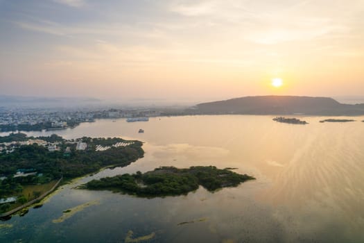 Aerial drone shot dawn dusk cityscape of Udiapur Rajasthan India with blue pink purple water of lake pichola fateh sagar towards aravalli mountains on foggy morning in India