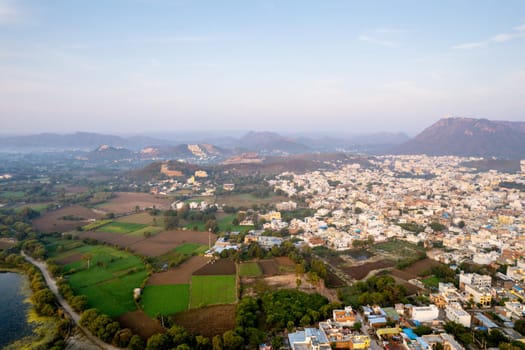 Aerial drone shot over udiapur, jaipur, kota,, cityscape with homes, houses, buildings and aravalli hills and lakes before sunrise and fog in distance in India