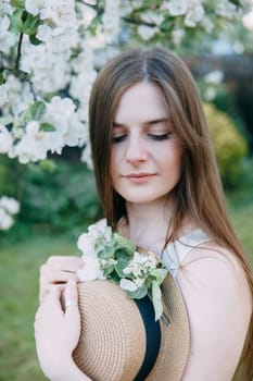 Beautiful young girl in white dress and hat in blooming Apple orchard. Blooming Apple trees with white flowers