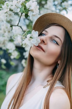 Beautiful young girl in white dress and hat in blooming Apple orchard. Blooming Apple trees with white flowers