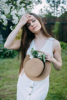 Beautiful young girl in white dress and hat in blooming Apple orchard. Blooming Apple trees with white flowers