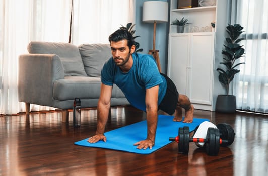 Flexible and dexterity man in sportswear doing yoga position in meditation posture on exercising mat at home. Healthy gaiety home yoga lifestyle with peaceful mind and serenity.