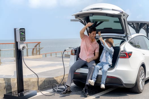 Family road trip vacation traveling by the sea with electric car, father and son recharge EV car with green and clean energy. Natural travel and eco-friendly car for sustainable environment. Perpetual