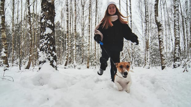 A girl and her Jack Russell Terrier dog are running through the woods