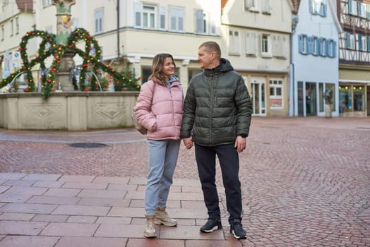 Loving couple of tourists walking around old town. Man woman couple walking europe old town Germany. Couple of lovers leisurely stroll in the cool autumn morning on the streets of a BIETIGHEIM-BISSINGEN (Germany). The guy holds his wife. Vacation, autumn, holiday. Couple Walking in Europe's Old Town