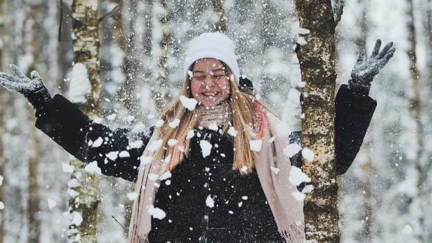 A girl is walking through the woods and kicking up snow in a birch forest