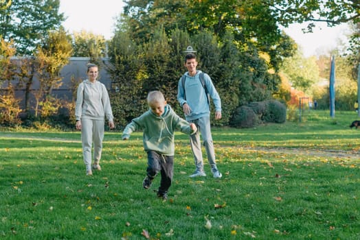 a family mom and 2 sons are having fun, running in the park and jumping. Sons, children, mom, run, play, rejoice, enjoy nature in summer. Family teamwork. Happy family team, running together in field, happily waving their hands. Group of people of different ages. happy family, mom and two sons on an emotional walk. Running and enjoying life in a green field in the park, blue sky, nature.