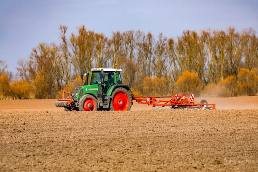 On an brown agricultural field, the arable land is being plowed by a tractor with a plough