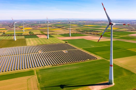 Generation of green energy in Germany by solar panels of a solar park and wind turbines up to the horizon as an aerial view