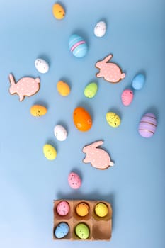 Beautiful decorative multicolored eggs and pink gingerbread in the form of rabbit, scattered on a light blue background, top view. Vertical