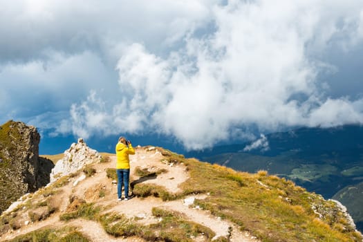 Woman takes photos of Seceda mountain standing on hill top overgrown with grass. Female tourist explores nature of Italian Alps aerial view