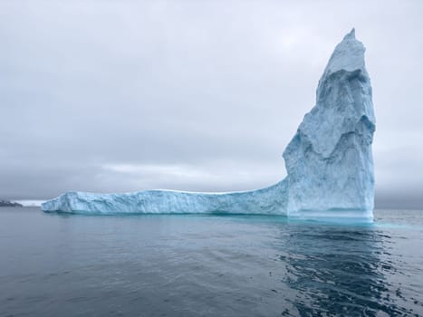 A huge high breakaway glacier drifts in the southern ocean off the coast of Antarctica at sunset, the Antarctic Peninsula, the Southern Arctic Circle, azure water, cloudy weather. High quality photo