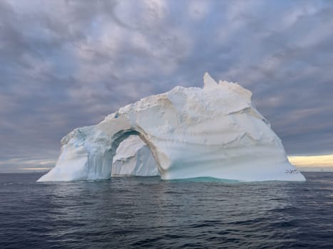 A huge high breakaway glacier drifts in the southern ocean off the coast of Antarctica at sunset, the Antarctic Peninsula, the Southern Arctic Circle, azure water, cloudy weather. High quality photo