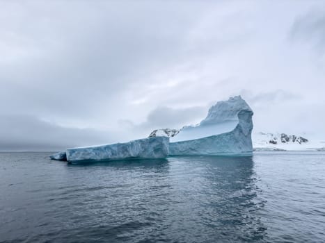 A huge high breakaway glacier drifts in the southern ocean off the coast of Antarctica at sunset, the Antarctic Peninsula, the Southern Arctic Circle, azure water, cloudy weather. High quality photo