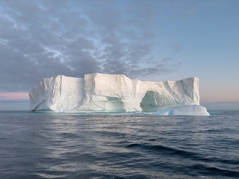 A huge high breakaway glacier drifts in the southern ocean off the coast of Antarctica at sunset, the Antarctic Peninsula, the Southern Arctic Circle, azure water, cloudy weather. High quality photo