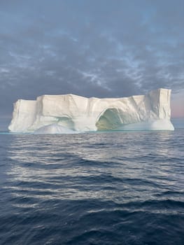 A huge high breakaway glacier drifts in the southern ocean off the coast of Antarctica at sunset, the Antarctic Peninsula, the Southern Arctic Circle, azure water, cloudy weather. High quality photo