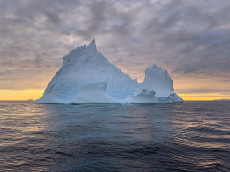 A huge high breakaway glacier drifts in the southern ocean off the coast of Antarctica at sunset, the Antarctic Peninsula, the Southern Arctic Circle, azure water, cloudy weather. High quality photo