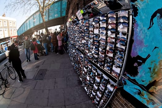 London, United Kingdom - April 01, 2007: Various sunglasses on display at street stall on Camden Market, famous flea market in UK capital, group of pedestrians in background. Fisheye photo