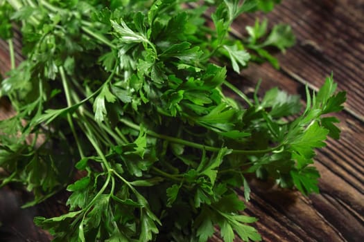 Green parsley leaves, used as herb in kitchen, on dark wooden board