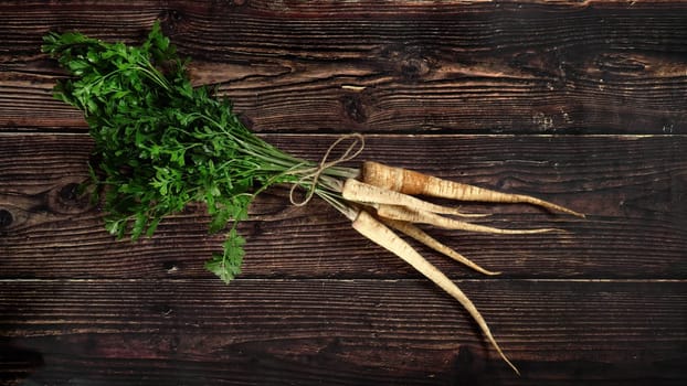 Bunch of parsnip roots with green leaves on rustic dark wooden board, view from above