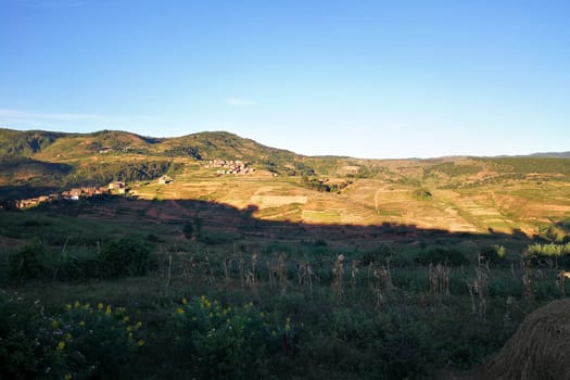 Typical Madagascar landscape in region near Alakamisy Ambohimaha, sun setting down over small clay houses, terraced rice fields in foreground and small hills background