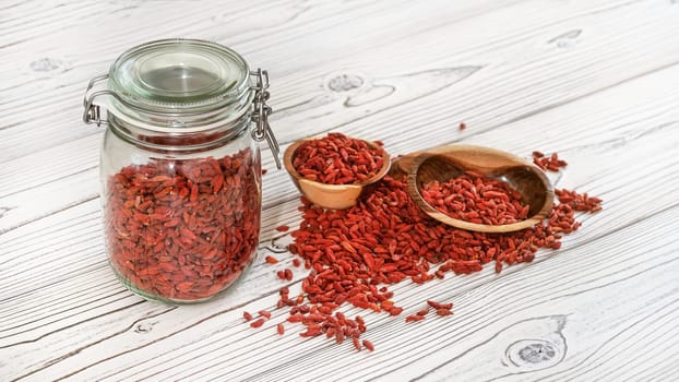 Dried goji aka. wolfberry seeds inside glass bottle, some in wooden bowls and spilled on white boards desk