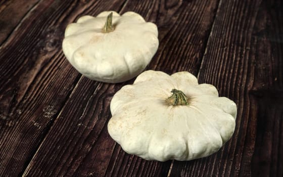 Two white pattypan squash on dark wooden board