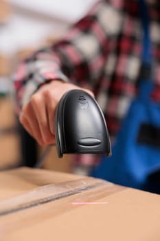 Delivery service employee scanning parcel and managing packages storing in warehouse. Storehouse worker doing shipment operations while holding barcode scanner in hand close up