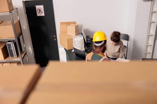 Diverse warehouse employees planning merchandise inventory, analyzing products checklist in storage room. Stockroom supervisor discussing clients orders with worker before start preparing packages