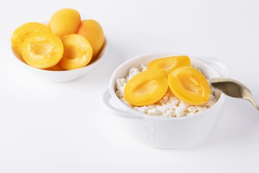 Fresh cottage cheese in white bowl with apricot pieces on white background.