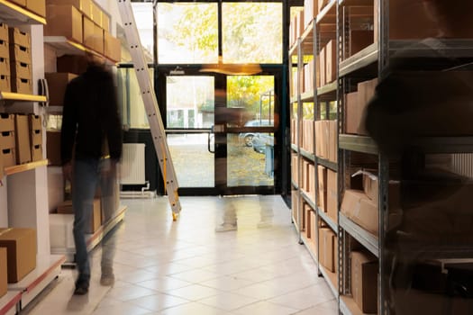 Diverse employees working in storehouse, preparing customers orders, putting products in cardboard boxes. African american worker wearing industrial overall in storage room. Blurred photo concept