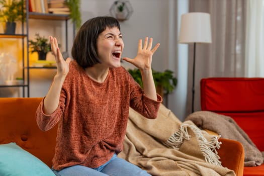 Sad woman feeling hopelessness loneliness, nervous breakdown, crying shouting while sitting on sofa in living room at home. Caucasian girl cries from despair, being sad because of unfair situation.