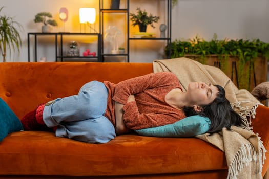 Upset young woman embracing belly suffering from stomachache lying on sofa. Unhappy Caucasian girl having menstrual painful feelings, resting on couch. Gastritis, abdominal or period pain concept