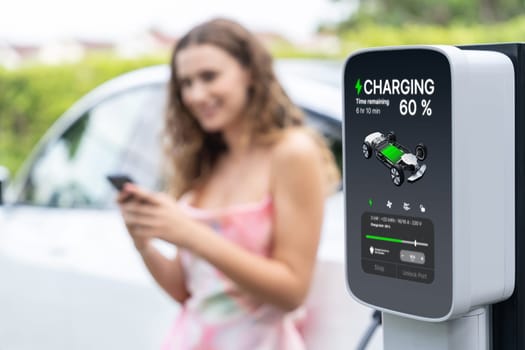 Focused outdoor charging station display EV car's battery charging status on blur background of woman using recharging electric vehicle for environmental friendly and future sustainability. Synchronos