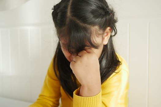 a upset child girl cover her face with hand .