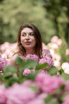 Hydrangeas Happy woman in pink dress amid hydrangeas. Large pink hydrangea caps surround woman. Sunny outdoor setting. Showcasing happy woman amid hydrangea bloom