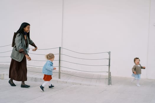 Smiling mother playing tag with little girls on a ramp near the house. High quality photo