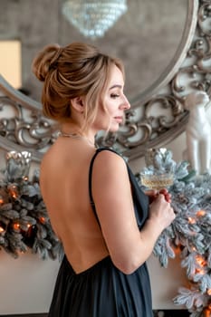 Portrait of a wealthy mature woman with evening make-up and hairstyle posing in a black dress on the background of the Christmas room. Luxurious lifestyle. Christmas holidays concept.