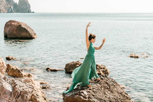 Woman green dress sea. Woman in a long mint dress posing on a beach with rocks on sunny day. Girl on the nature on blue sky background